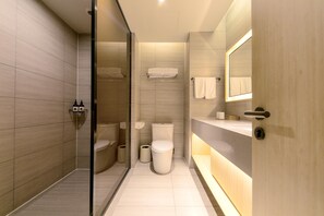 A modern bathroom with a glass shower enclosure, a toilet, a bidet, and a sink with a mirror. - Ji Hotel (Hangzhou)
