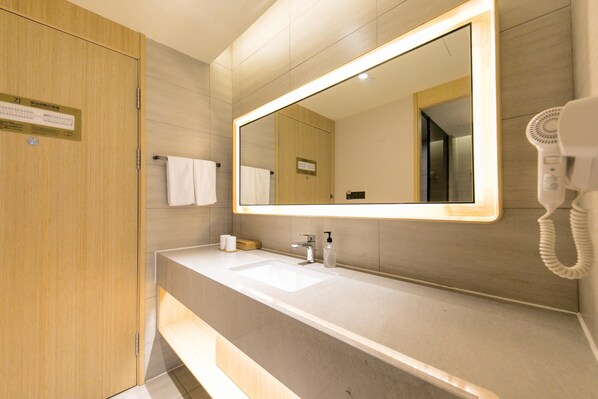 Un baño de hotel con un espejo grande, un lavamanos, un perchero para toallas y un secador de pelo.