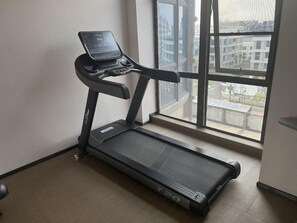 A treadmill in a room with a large window, a wooden floor, and a plain wall. - Ji Hotel (Hangzhou)