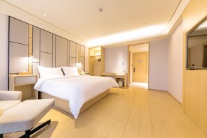 A modern hotel room with a large bed, bedside tables, a chair, a desk, and a mirror.