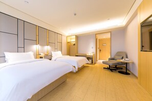 A hotel room with two beds, a desk, a chair, and a small table.