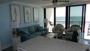 A room with a sofa, two armchairs, a dining table, a ceiling fan, and a view of the ocean. - Beachfront condo at Island Winds West in Gulf Shores (Gulf Shores)