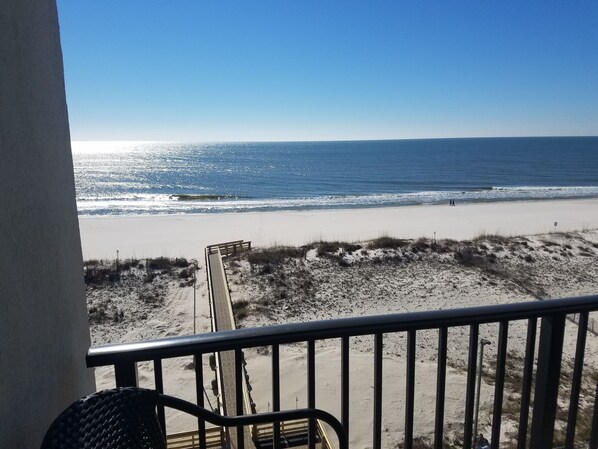 Une vue sur la plage depuis un balcon doté d’une terrasse en bois et d’une rambarde en métal.
