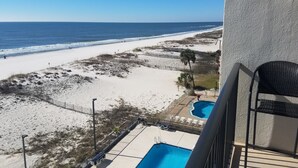 A balcony with a view of a beach, a swimming pool, and a fenced area with lounge chairs. - Beachfront condo at Island Winds West in Gulf Shores (Gulf Shores)