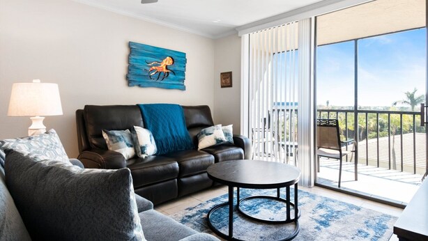 Un salon avec un canapé en cuir, une table basse ronde et une vue sur un balcon aménagé avec du mobilier d’extérieur.