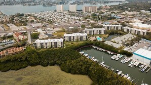 Vue aérienne d’une ville côtière avec de nombreux immeubles résidentiels, une marina où sont amarrés de nombreux bateaux, et une vaste étendue d’eau en arrière-plan.