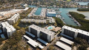 Une vue aérienne d’une marina où sont amarrés des bateaux, entourée de bâtiments résidentiels et bordée par une vaste étendue d’eau.
