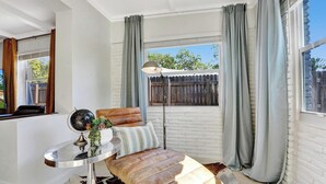 Una habitación acogedora con un sofá de cuero, un globo terráqueo sobre una mesita y vistas a una valla de madera a través de una ventana con cortinas grises.