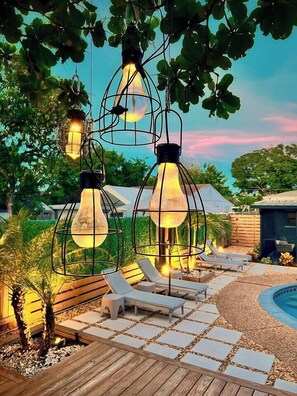A poolside area with lounge chairs, a wooden deck, and hanging light fixtures. - Stylish Pet Friendly Home with Private Pool Oasis (Fort Lauderdale)