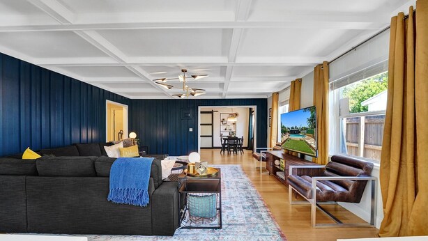 Una sala de estar moderna con paredes azul oscuro, piso de madera, un sofá oscuro, una mesa de centro, un televisor y un sillón de cuero.