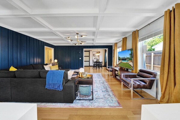 A modern living room with dark blue walls, a wooden floor, a dark sofa, a coffee table, a TV, and a leather armchair.