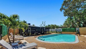 Un patio trasero con piscina, sillas de descanso y una casa moderna.