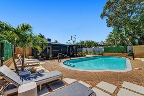 A backyard with a swimming pool, lounge chairs, and a modern house.