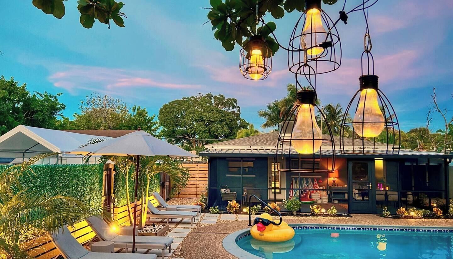 A pool area with lounge chairs, a pool, and hanging light fixtures.
