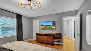Un dormitorio con cama, un armario de madera, un televisor en la pared y una puerta que da a otra habitación.