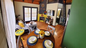 A cozy living room with a fireplace, a dining area with a table set for two, and a kitchen with a TV and a mirror.