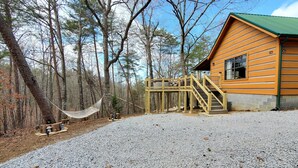 A wooden cabin with a gravel driveway, a wooden deck, and a hammock.