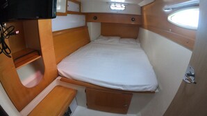 A compact, well-lit room with a bed, a small bench, a TV mounted on the wall, and a window providing natural light. - BoraBora Cruising Trip (Bora-Bora)