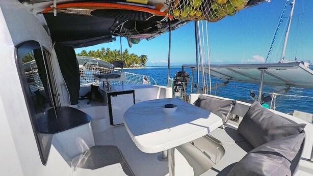 A boat deck with a table and cushioned seating, a netted area, and a view of the sea and palm trees. - BoraBora Cruising Trip (Bora-Bora)