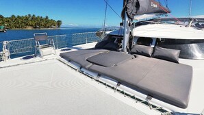 A yacht deck with a lounge area, a netted swimming area, and a view of a tropical island. - BoraBora Cruising Trip (Bora-Bora)