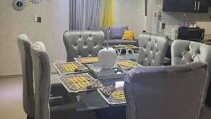 A dining area with a glass-top table, grey upholstered chairs, and a chandelier.