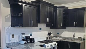 A modern kitchen with dark cabinets, a granite countertop, a gas stove, and two bar stools.
