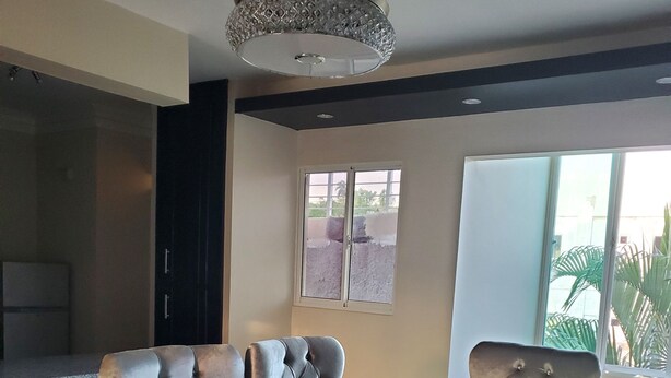 A modern dining area with a glass-top table, tufted leather chairs, and a decorative ceiling light.