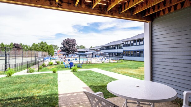 A covered patio area with a table and chairs, a swimming pool, and a building in the background. - Nautical Mile (Wells)