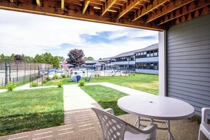 A covered patio area with a table and chairs, a swimming pool, and a building in the background. - Nautical Mile (Wells)