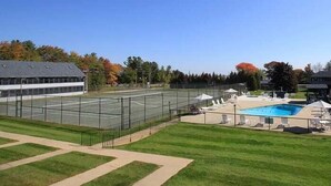 A tennis court adjacent to a swimming pool with lounge chairs and umbrellas. - Nautical Mile (Wells)