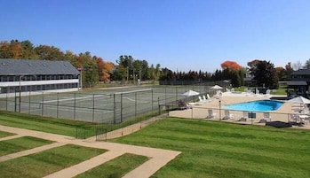 A tennis court adjacent to a swimming pool with lounge chairs and umbrellas.
