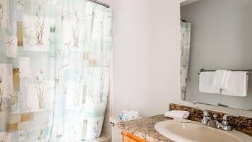 Une salle de bain avec un rideau de douche orné d’un motif naturel, un lavabo avec un plan de travail en granit et un miroir au-dessus du lavabo.