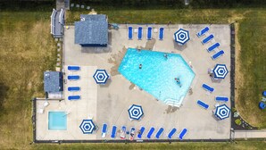 An aerial view of a swimming pool area with multiple sun loungers and umbrellas, surrounded by a grassy area and a building structure. - Nautical Mile (Wells)