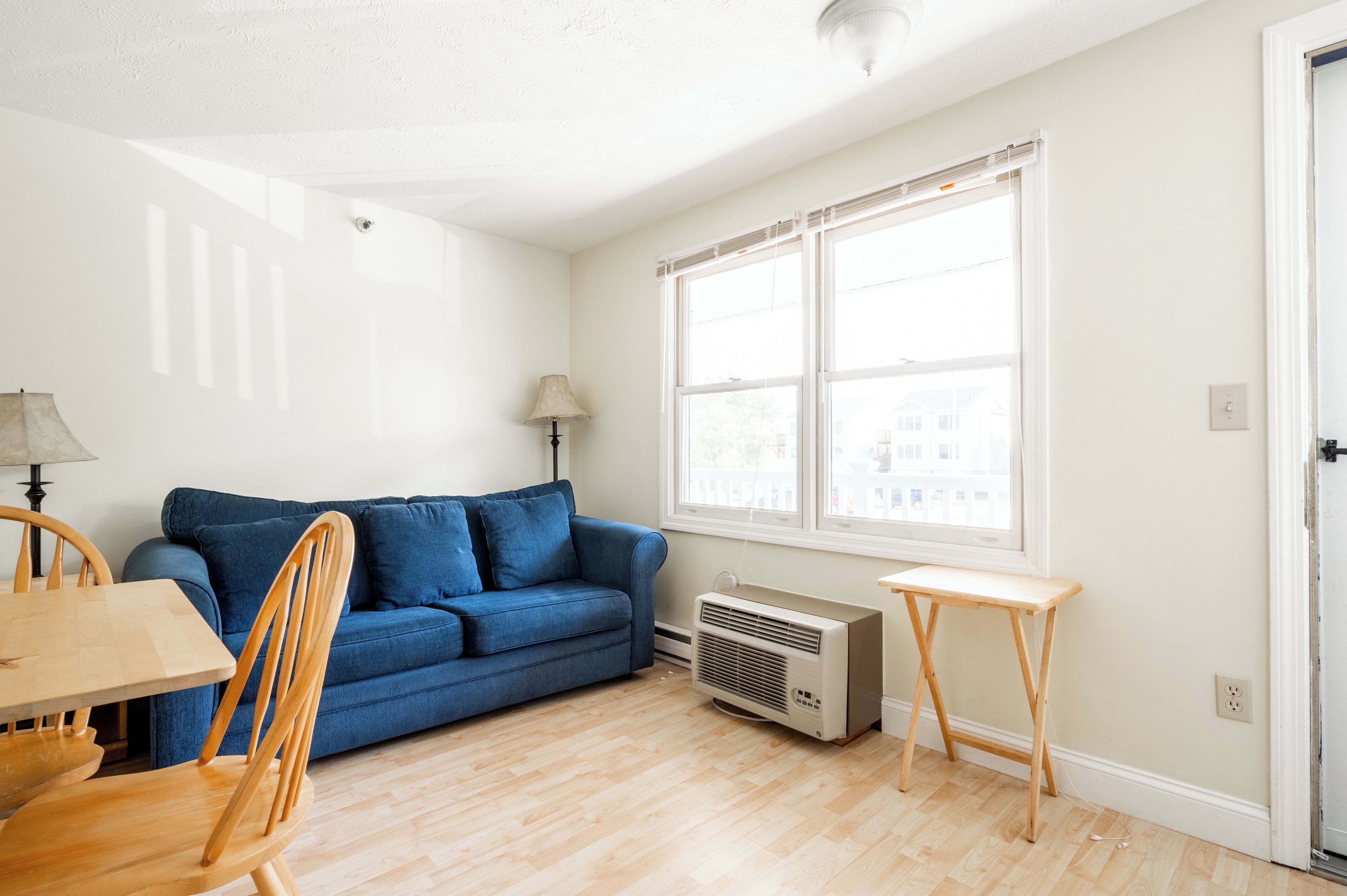 Un salon avec un canapé bleu, des chaises en bois, une petite table et un radiateur portatif.