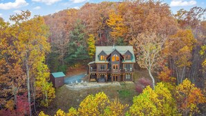 A log cabin with a wrap-around porch and a stone fireplace, surrounded by autumn foliage. - Family-Friendly Blue Ridge Log Cabin w Stunning Views-Free Flexible Check In-Out (Blue Ridge)
