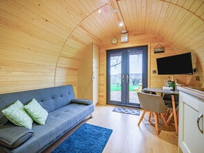 L’intérieur chaleureux d’un chalet avec un canapé, une table à manger et un téléviseur fixé au mur.