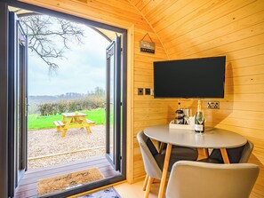 Ein modernes Zimmer mit Holzvertäfelung, einem großen Fenster, einem Flachbildfernseher, einem runden Tisch mit Stühlen und einem Picknicktisch draußen.