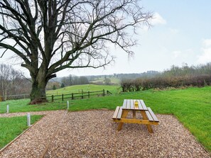Una mesa de picnic en un área con césped y un árbol grande al fondo.
