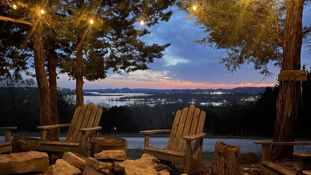 Järvenrantainen oleskelualue, jossa on Adirondack-tyylisiä tuoleja, kivinen nuotiopaikka ja valoketju.