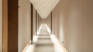 Ein langer, schmaler Korridor mit einem gemusterten Boden, Türen an beiden Seiten und Einbaustrahlern in der Decke.