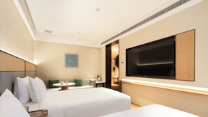 Ein Hotelzimmer mit zwei Betten, einem Fernseher, einem kleinen Tisch und einem an der Wand montierten Fernseher.