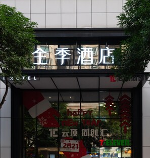 A hotel entrance with a sign in Chinese characters, a 'Happy New Year 2021' banner, and a '7-Eleven' store in the background.