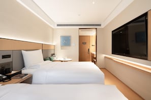 A hotel room with two beds, a desk with a telephone, a small table with a cup and saucer, and a television on the wall. - Ji Hotel (Guangzhou)