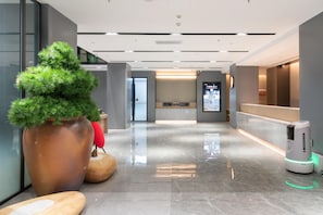 A modern lobby with a reception desk, a large potted plant, a robotic vacuum cleaner, and a polished marble floor. - Ji Hotel (Guangzhou)