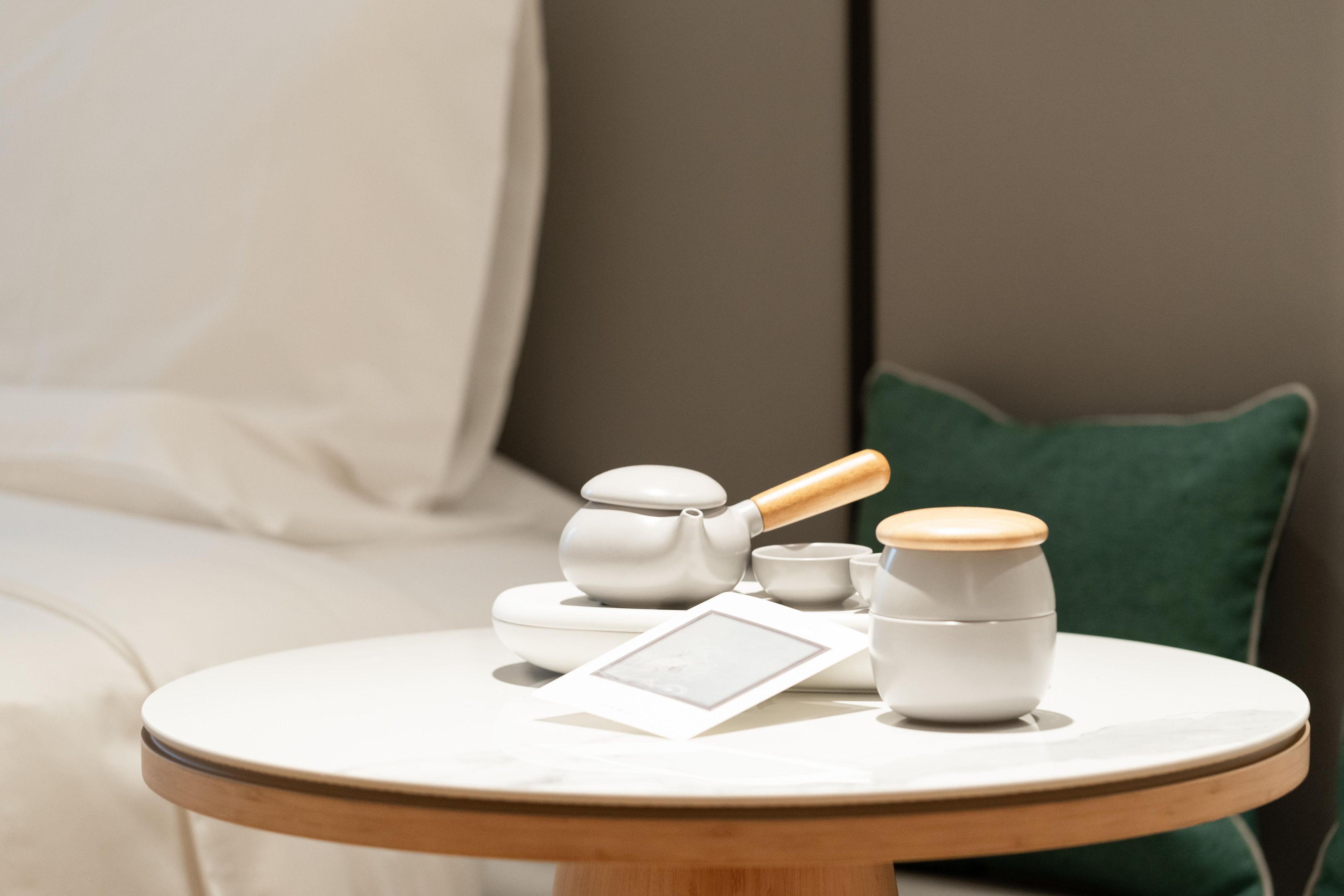 A round table with a white teapot, a cup, and a small bowl, accompanied by a framed picture.