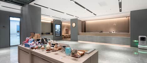 A modern hotel lobby with a reception desk, a digital display, and a self-service kiosk.