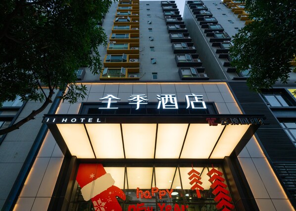 A hotel entrance with a sign in both English and Chinese, a large illuminated sign with 'HAPPY NEW YEAR,' and a modern building facade with multiple balconies.