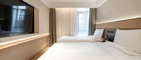 A hotel room with two beds, a TV, a bedside table, and a window with curtains.