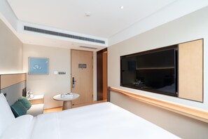 A modern hotel room with a large bed, a bedside table, a small round table, a built-in TV, and a large window. - Ji Hotel (Guangzhou)