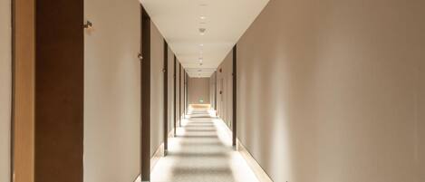 A long, narrow hallway with a patterned floor, doors on both sides, and recessed lighting on the ceiling.